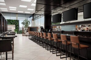 A modern bar area with high tables and bar stools, large windows, and a visible bar counter with various bottles. - Marriott Indianapolis East (Indianapolis)