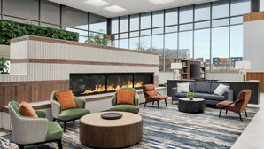 A spacious lounge area with a fireplace, comfortable seating, and large windows offering views of the city. - Marriott Indianapolis East (Indianapolis)
