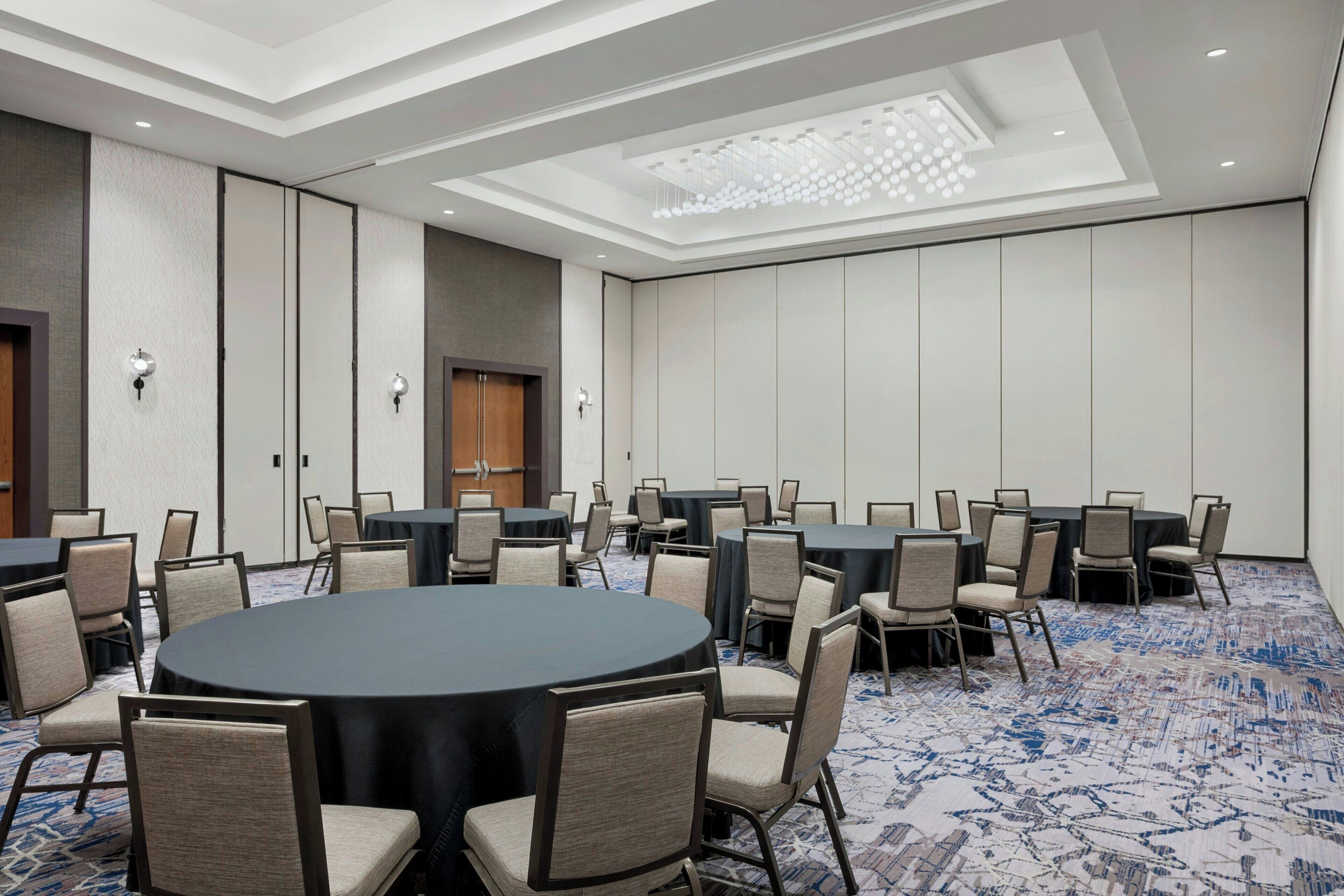 A conference room with round tables and chairs, a patterned carpet, and a ceiling with recessed lighting.