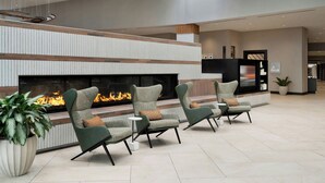 A modern lounge area with a fireplace, green upholstered chairs, and a large potted plant. - Marriott Indianapolis East (Indianapolis)