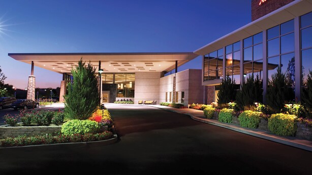 A Marriott hotel entrance with a covered walkway, large windows, and landscaped areas with shrubs and flowers. - Marriott Indianapolis East (Indianapolis)