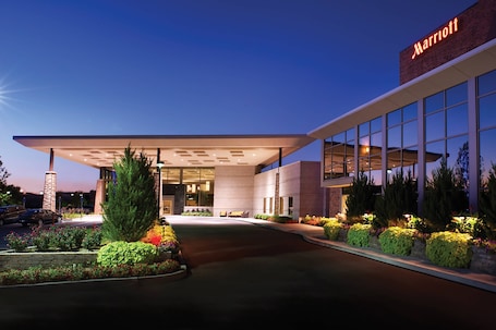 A Marriott hotel entrance with a covered walkway, large windows, and landscaped areas with shrubs and flowers.