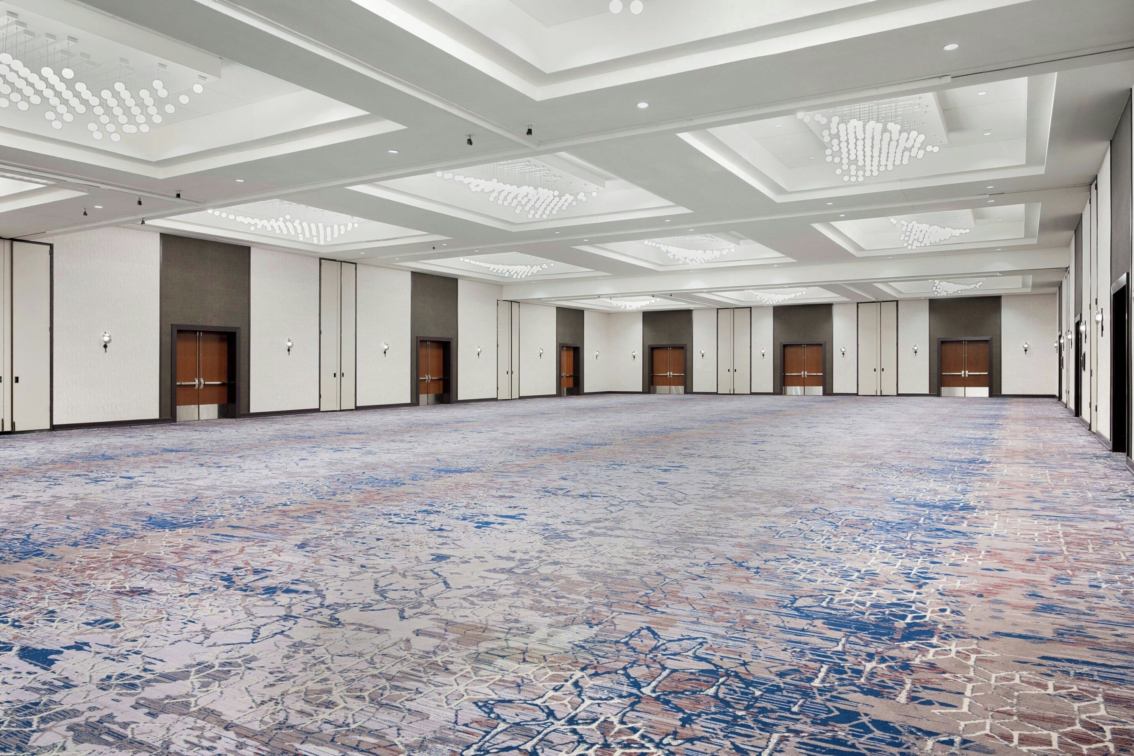 A spacious hotel lobby with a patterned floor, recessed lighting, and a row of doors.