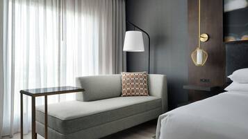Una habitación de hotel moderna con un sofá gris, una mesita, una lámpara y una cama.