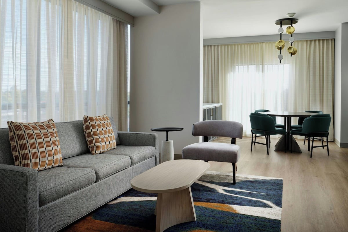 A modern living room with a grey sofa, matching armchair, and a round coffee table. There is a dining area with a table and chairs.