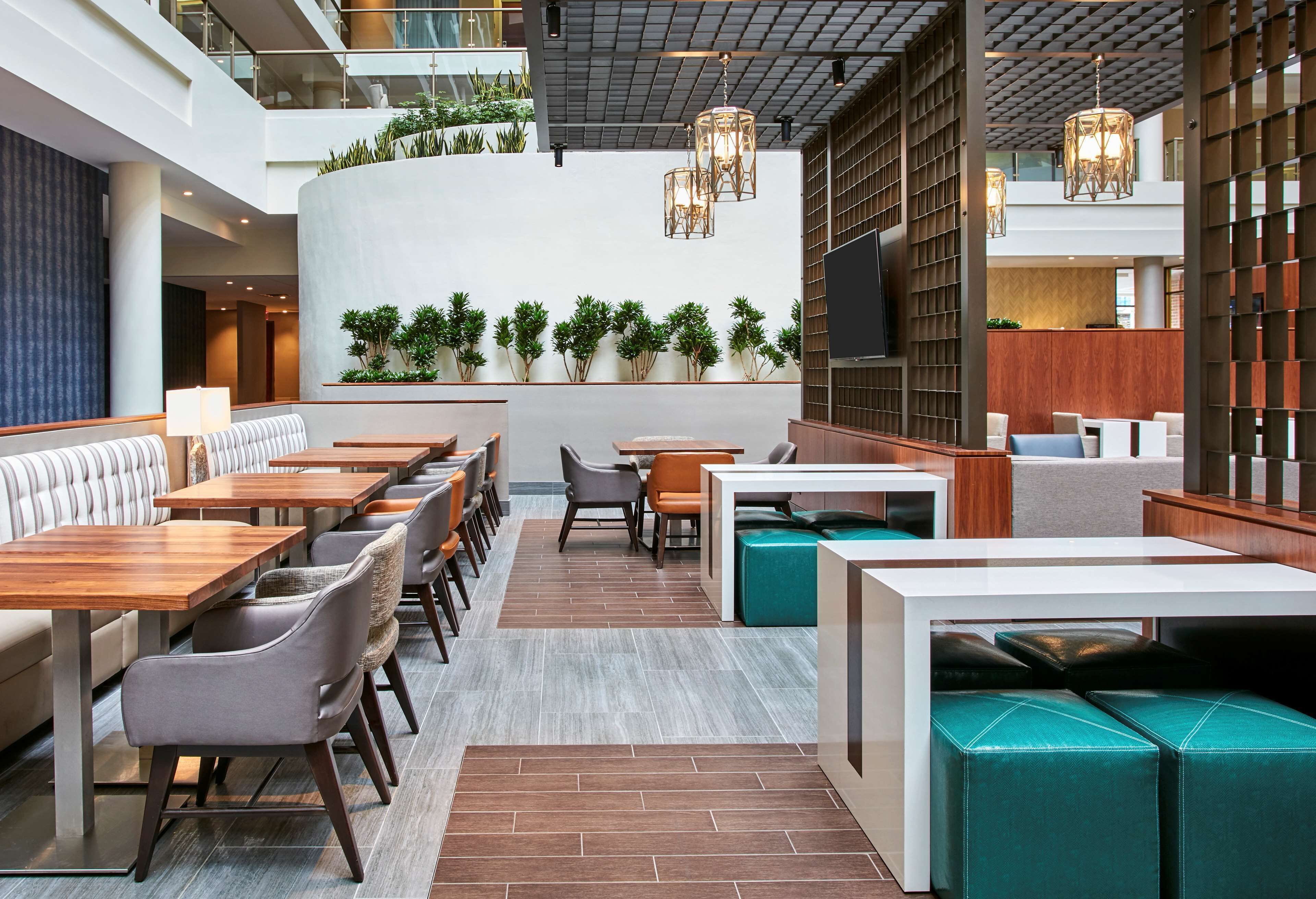 A modern restaurant with high tables, cushioned seating, and a central planter wall.