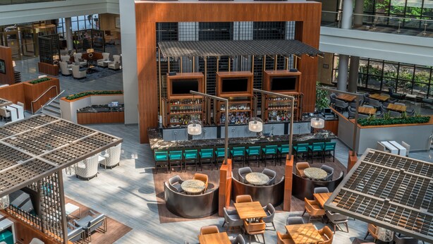 A spacious indoor area with multiple seating arrangements, including tables and chairs, and a central bar area with shelves of bottles. - Embassy Suites by Hilton Washington DC Georgetown (Washington)