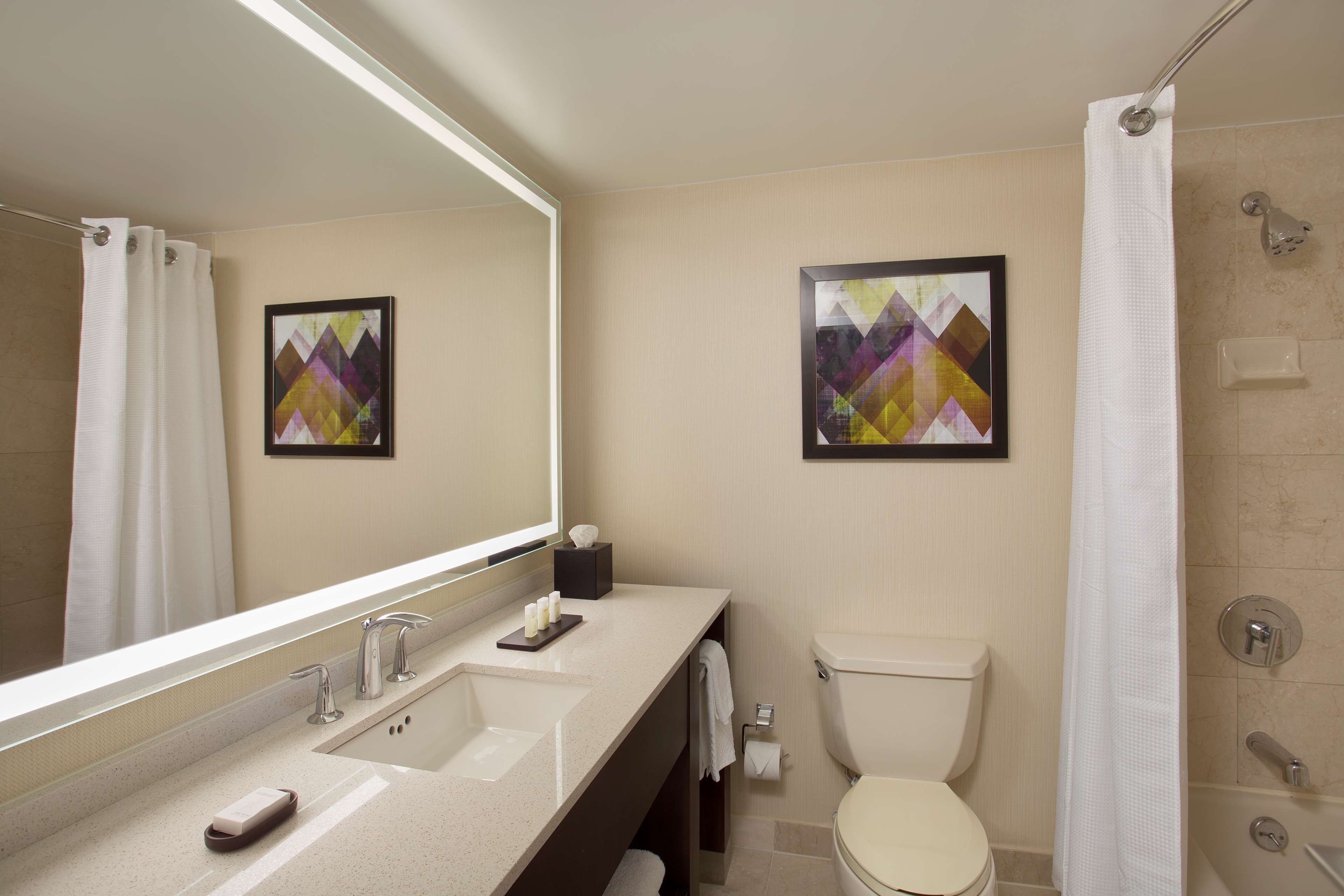 A modern bathroom with a large mirror, a sink with two faucets, a toilet, and a shower area.