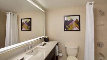 A modern bathroom with a large mirror, a sink with two faucets, a toilet, and a shower area.