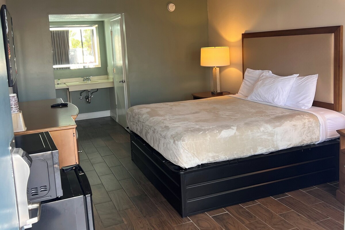 Een hotelkamer met een bed, een bedlampje, een spiegel, een raam en een kitchenette.