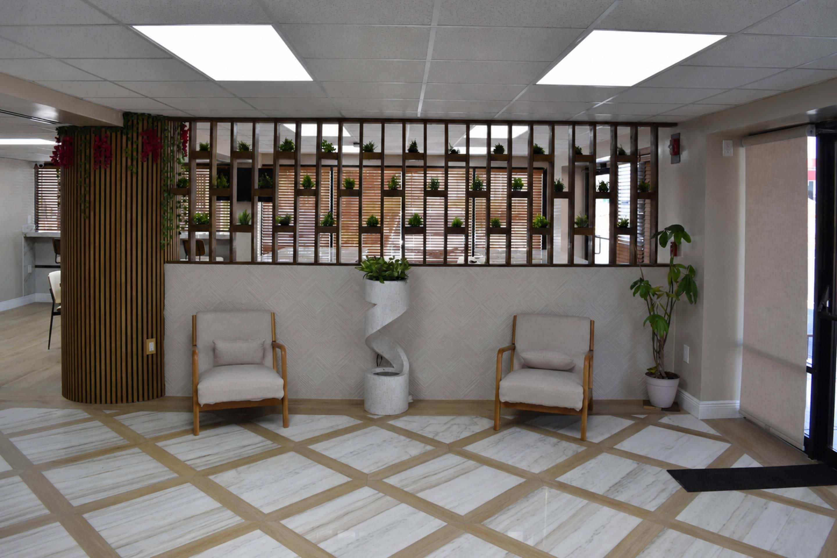 Un área de recepción con dos sillas, una planta decorativa y un piso con diseño.