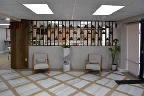 A reception area with a check-in counter, two armchairs, a potted plant, a decorative wall with vertical slats, and a patterned floor. - Rodeway Inn Davenport-Champions Gate (Davenport)