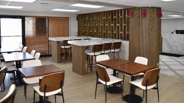 Ein Restaurant mit Holztischen und -stühlen, einer Theke und einer Wand mit Pflanzen als Dekoration.