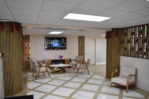 A modern hotel lobby with a central seating area, a television, and decorative plants.