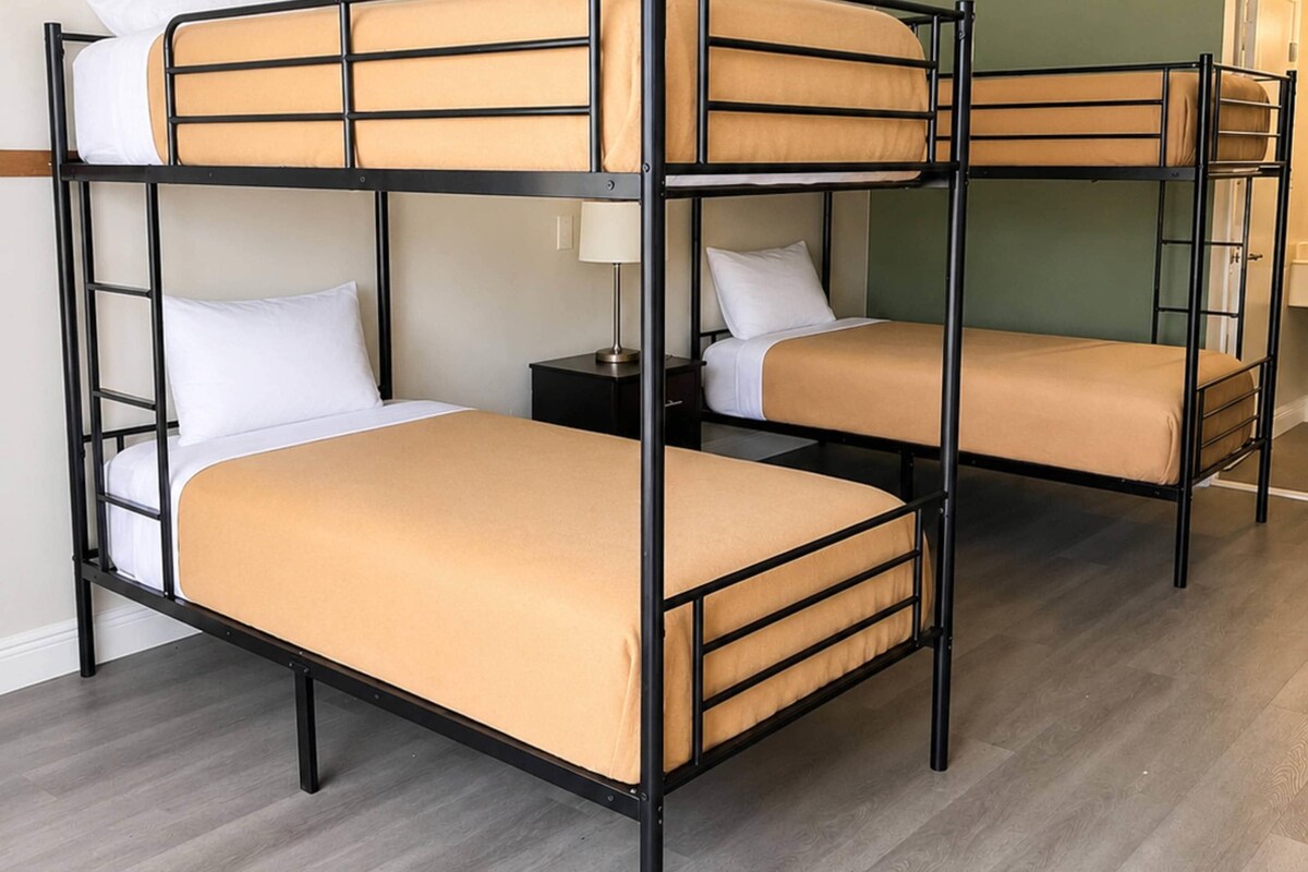 Een slaapkamer met stapelbed, houten vloer, nachtkastje met lamp en groene wand.