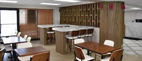 Un restaurante con mesas y sillas de madera, una barra y una pared decorativa con plantas.