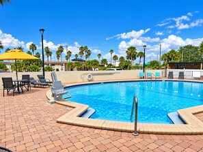 A swimming pool with lounge chairs and umbrellas, surrounded by palm trees and a clear sky. - Rodeway Inn Davenport-Champions Gate (Davenport)