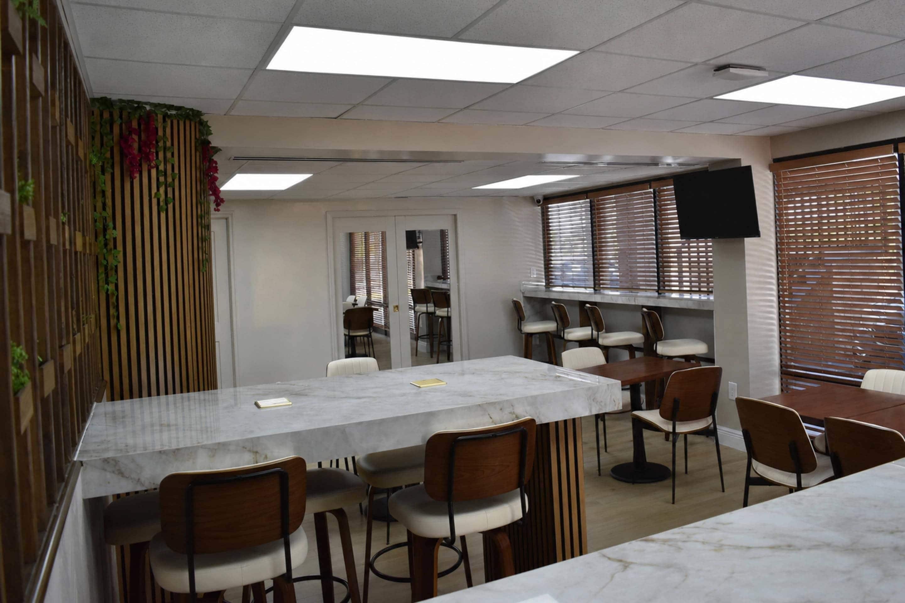 A conference room with a marble table, wooden chairs, a television, and a window with blinds.