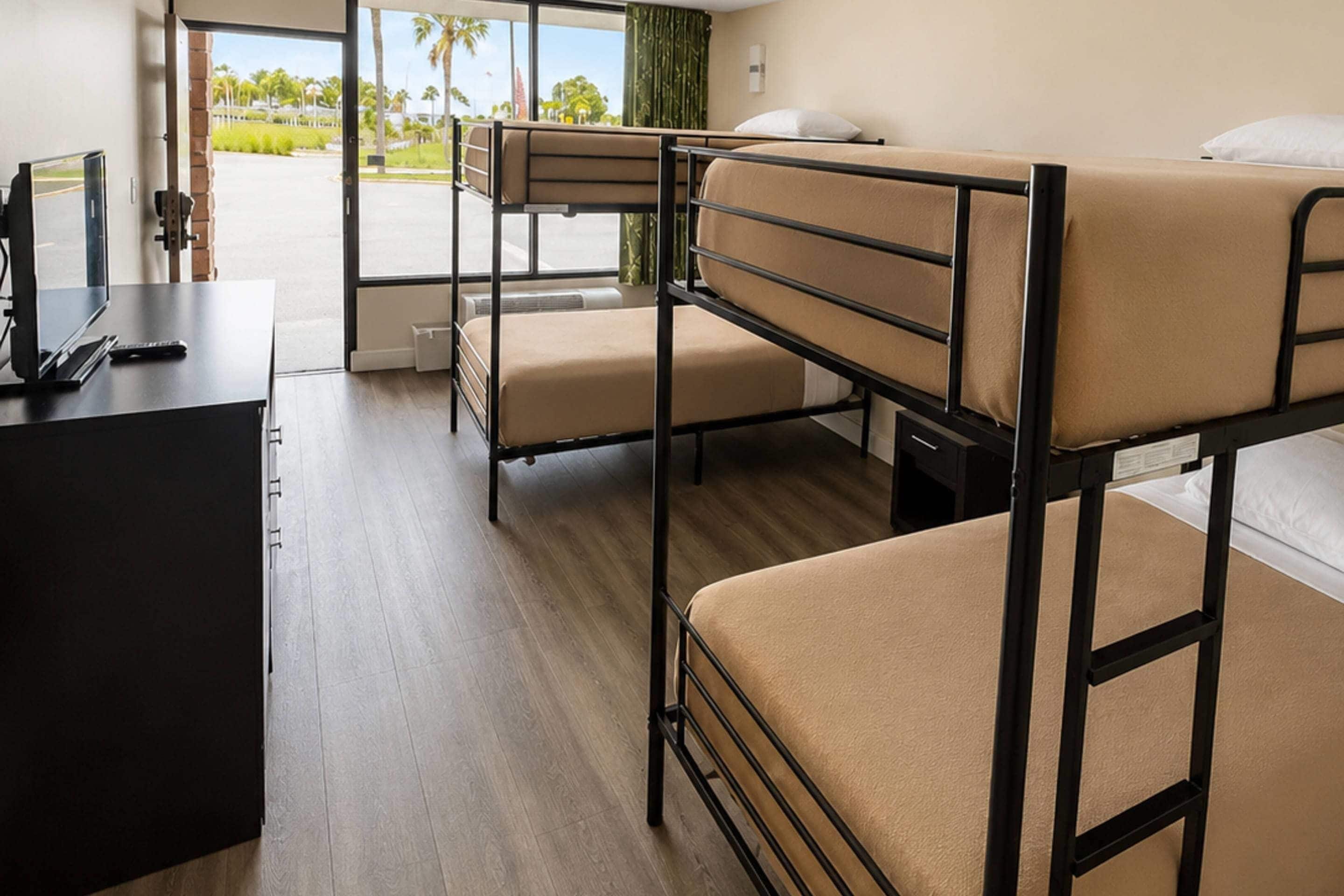 A room with bunk beds, a desk with a computer, and a window with a view of palm trees.