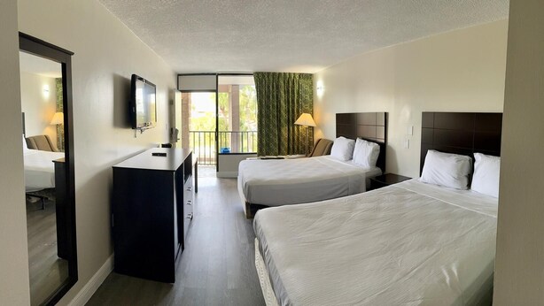 A hotel room with two beds, a desk, a TV, and a balcony with a view.
