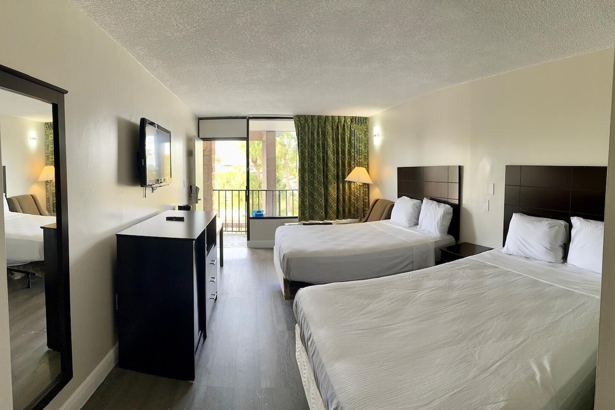 Een hotelkamer met twee bedden, een bureau, een televisie en een balkon met uitzicht.