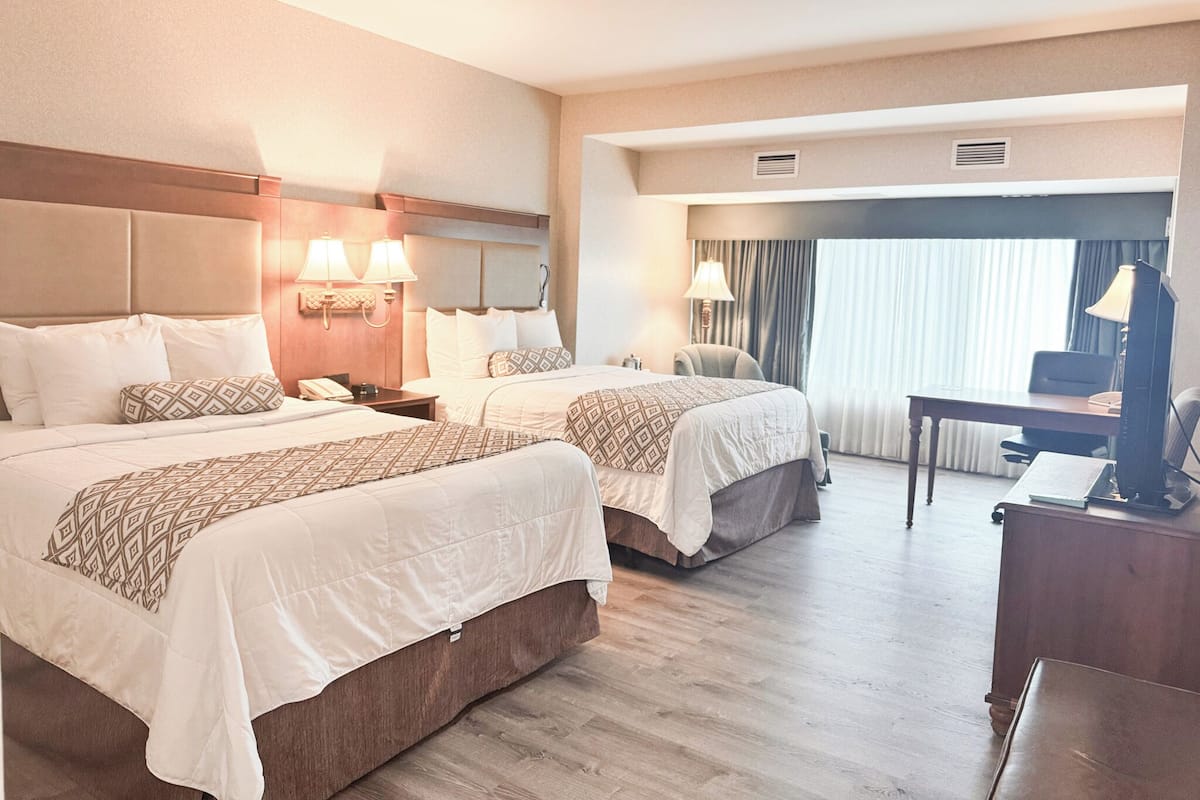 Ein Hotelzimmer mit zwei Betten, einem Schreibtisch, einem Stuhl und einem Fernseher.