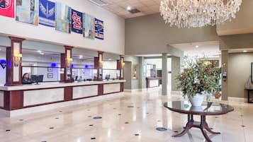 A hotel lobby with a reception desk, a chandelier, and artwork on the wall.