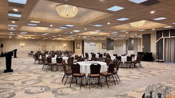 A large conference room with multiple round tables, chairs, and a podium.
