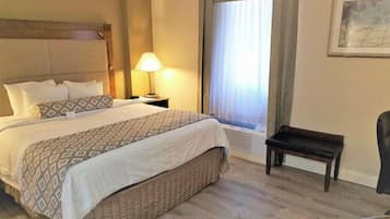 A hotel room with a bed, bedside table, lamp, window with curtains, and a chair.