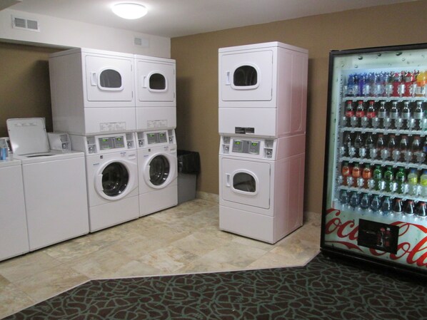 Un área de lavandería con lavadoras y secadoras apiladas, y un refrigerador Coca-Cola.