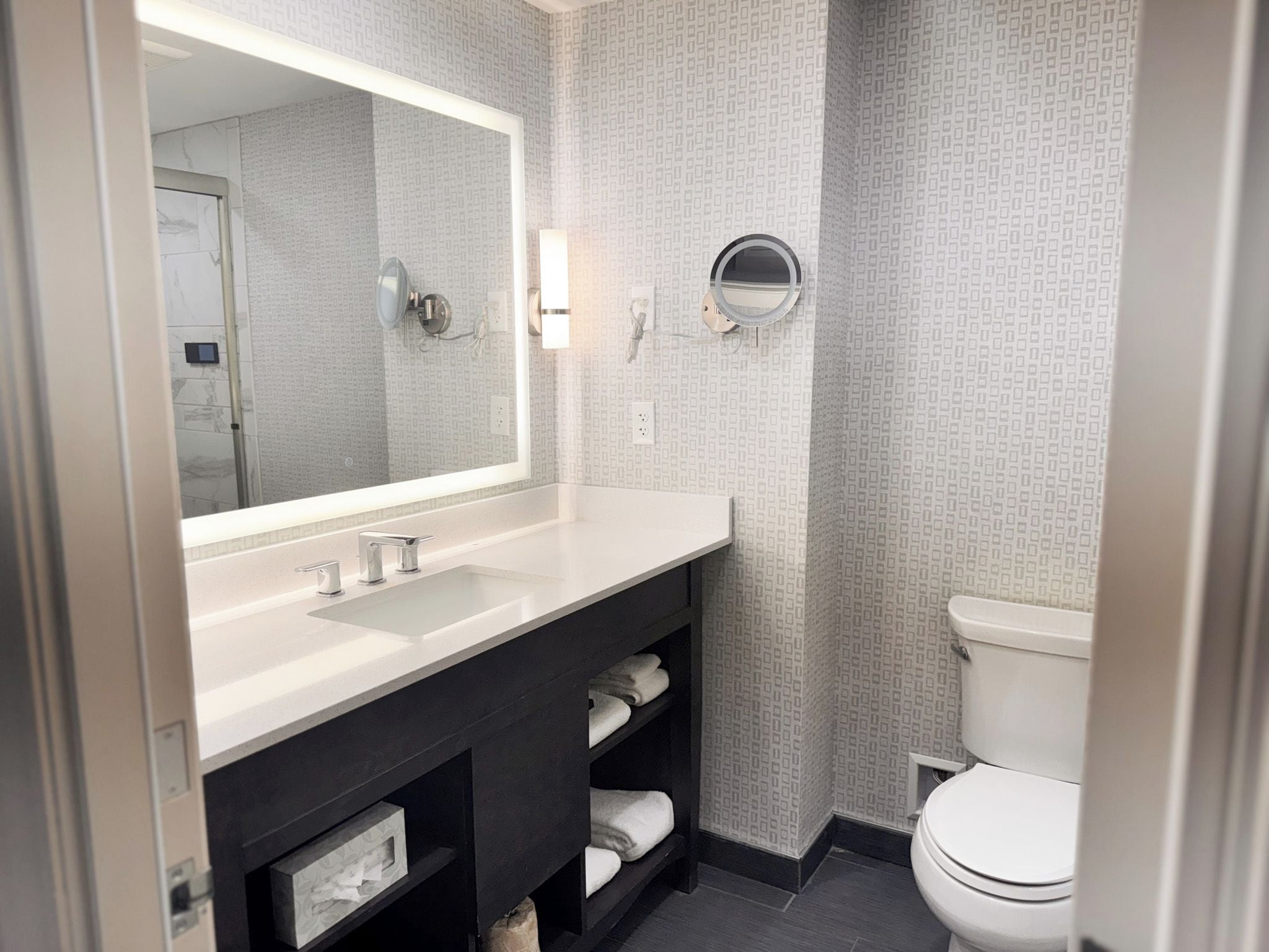 A modern bathroom with a white vanity, a large mirror, a toilet, and a towel rack.
