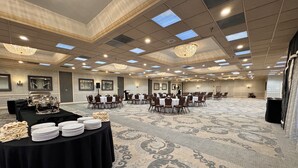 A large conference room with rows of tables and chairs, a podium, and a buffet table with plates and napkins. - Clayton Plaza Hotel & Extended Stay (St. Louis)
