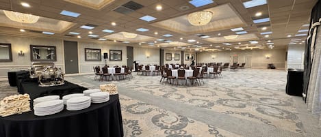 A large conference room with rows of tables and chairs, a podium, and a buffet table with plates and napkins.