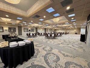 Une grande salle de conférence avec des rangées de tables et de chaises, un pupitre et une table de buffet garnie d  ’assiettes et de serviettes.
