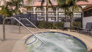 A hot tub with metal railings, surrounded by palm trees and a fence, with a building in the background.