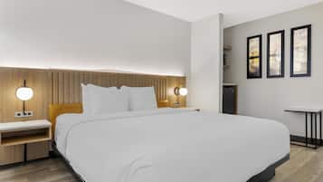 A modern hotel room with a large bed, wooden headboard, bedside tables with lamps, and a small desk with a chair.