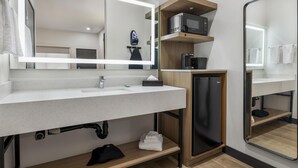 A modern bathroom with a white sink, a mirror, a black refrigerator, and a microwave on a shelf.