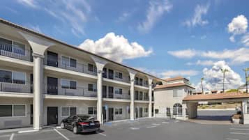 A multi-story hotel with balconies, a parking lot, and a clear sky.