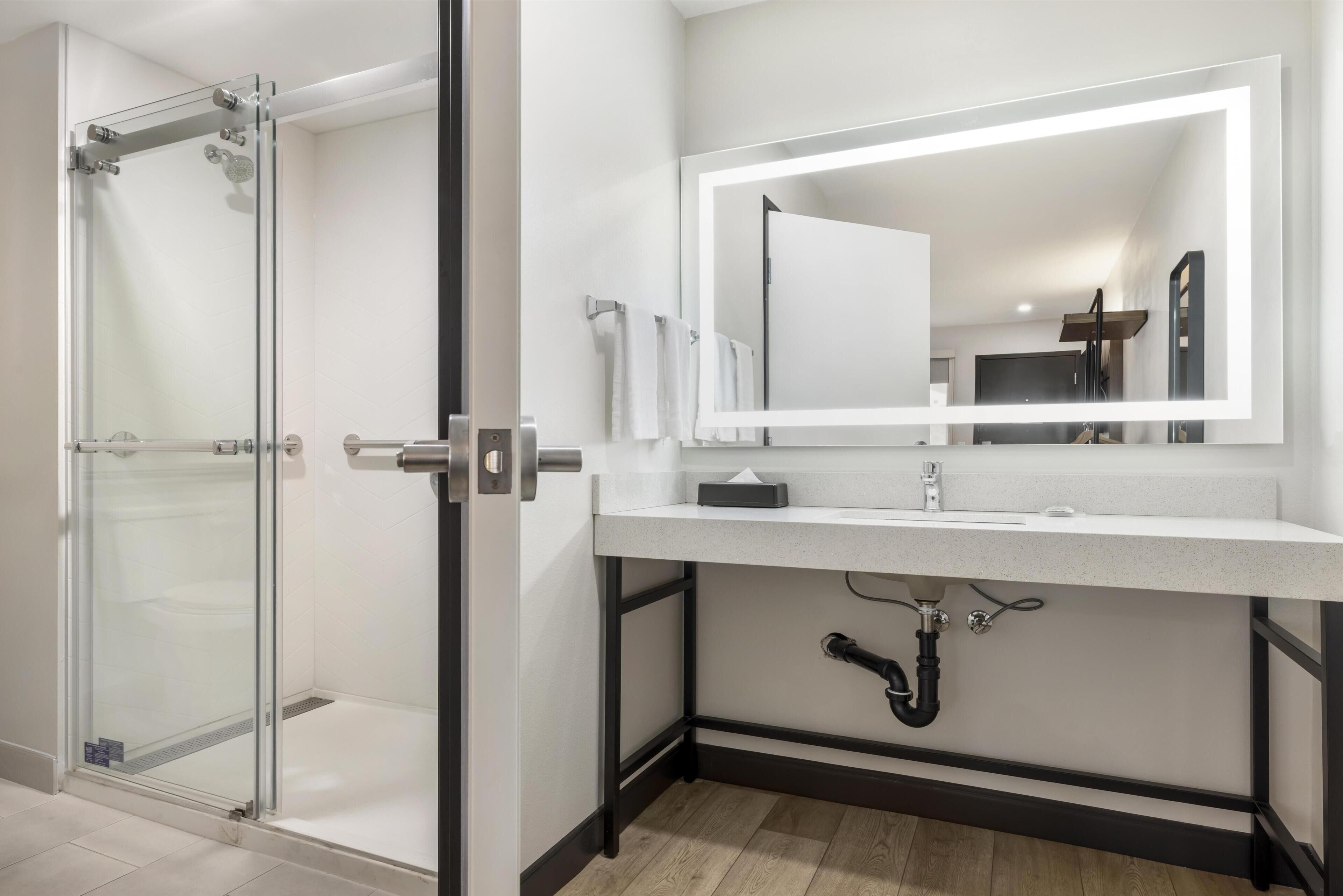 A modern bathroom with a glass shower enclosure, a white sink with a large mirror, and a black frame around the sink.