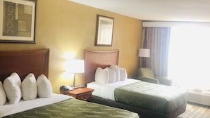 Habitació d'hotel amb dos llits, un capçal de llit de fusta, una tauleta de nit, una làmpada i una finestra amb cortines.