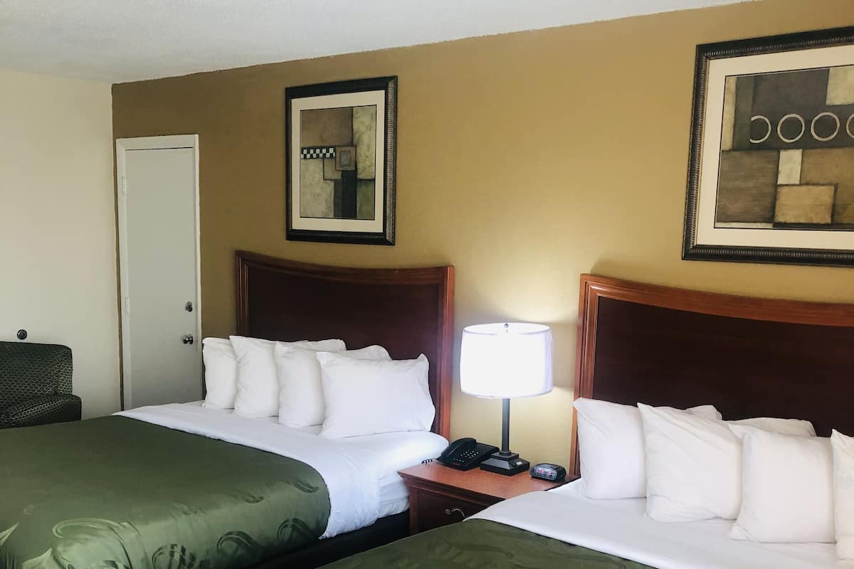 Une chambre d’hôtel avec deux lits, une table de chevet avec une lampe, un téléphone et des œuvres d’art accrochées aux murs.