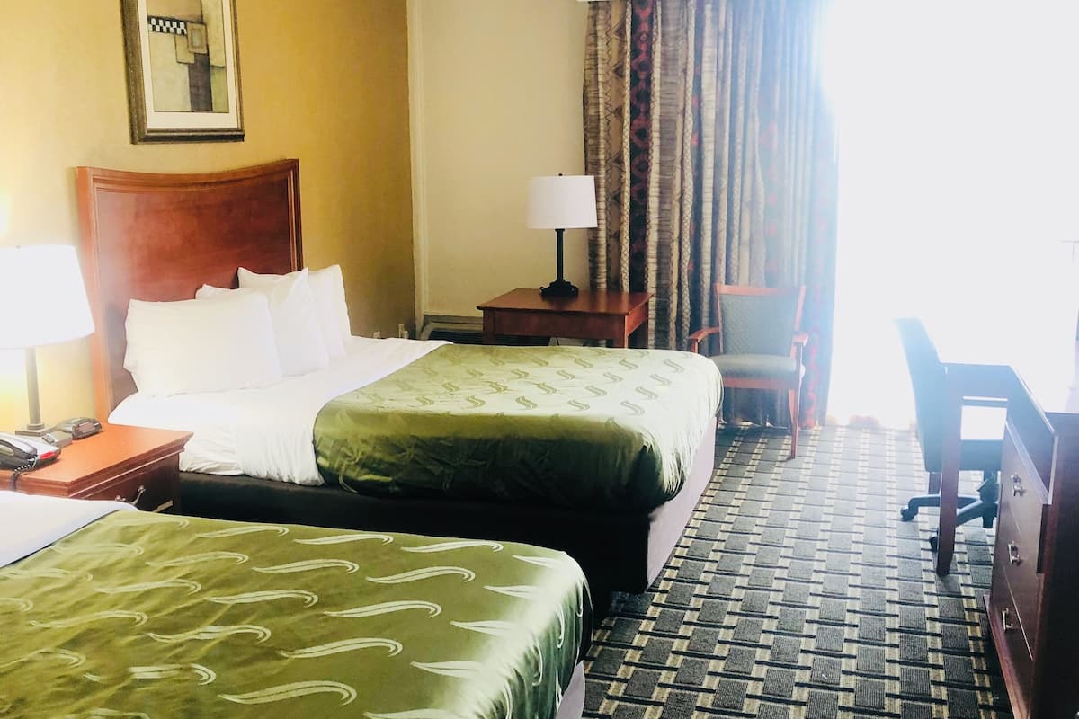 Une chambre d’hôtel avec deux lits, un bureau, une chaise et une lampe.