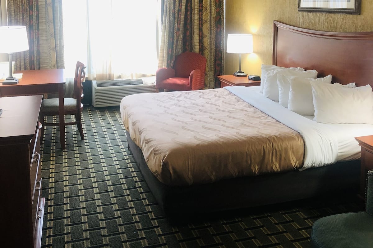 Une chambre d’hôtel avec un grand lit, deux tables de chevet, un bureau, une chaise et une fenêtre avec des rideaux.