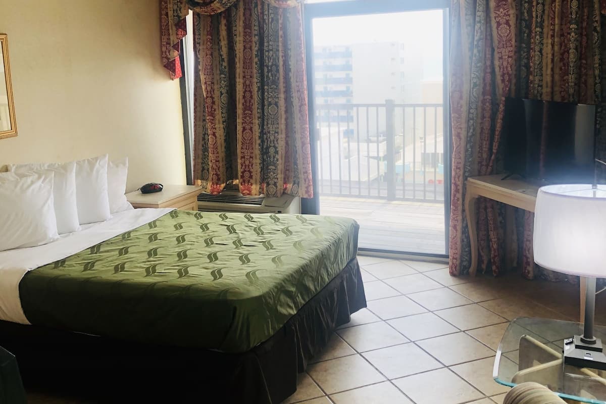 Une chambre d’hôtel avec un lit, une chaise, un bureau, une télévision et un balcon avec des rideaux.