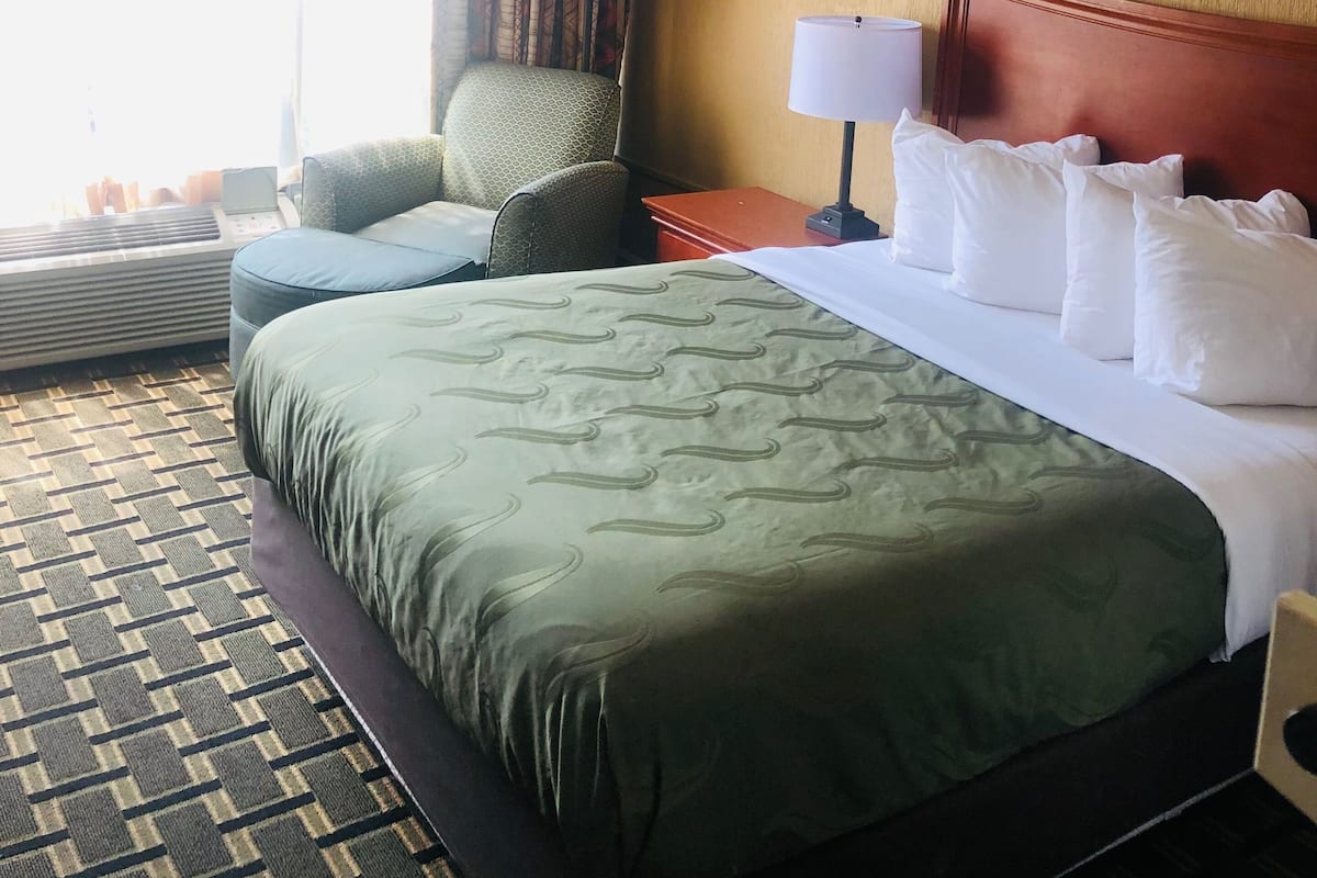Une chambre d’hôtel avec un grand lit, un bureau, une chaise et une fenêtre avec des rideaux.