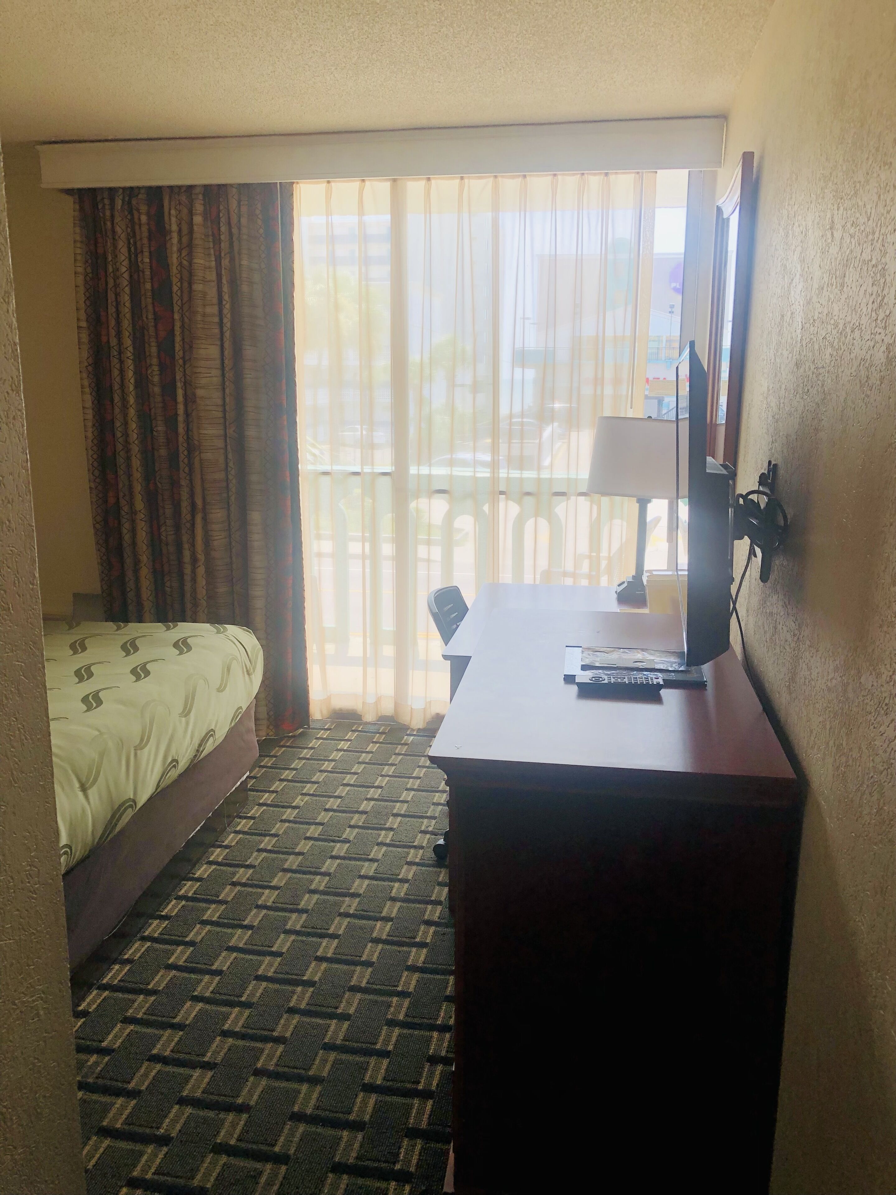 A hotel room with a bed, a desk with a lamp, a chair, and a window with curtains.
