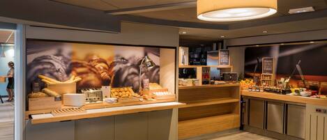 A modern café with a wooden counter displaying pastries and a coffee station.