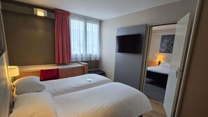 A hotel room with a bed, bedside table, lamp, TV, and a door leading to another room. - ibis Tours Nord (Tours)