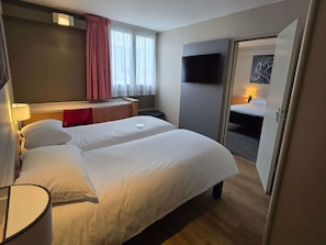 A hotel room with a bed, bedside table, lamp, TV, and a door leading to another room. - ibis Tours Nord (Tours)