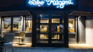 A bistro with a neon sign, glass doors, and wicker chairs outside. - ibis Tours Nord (Tours)